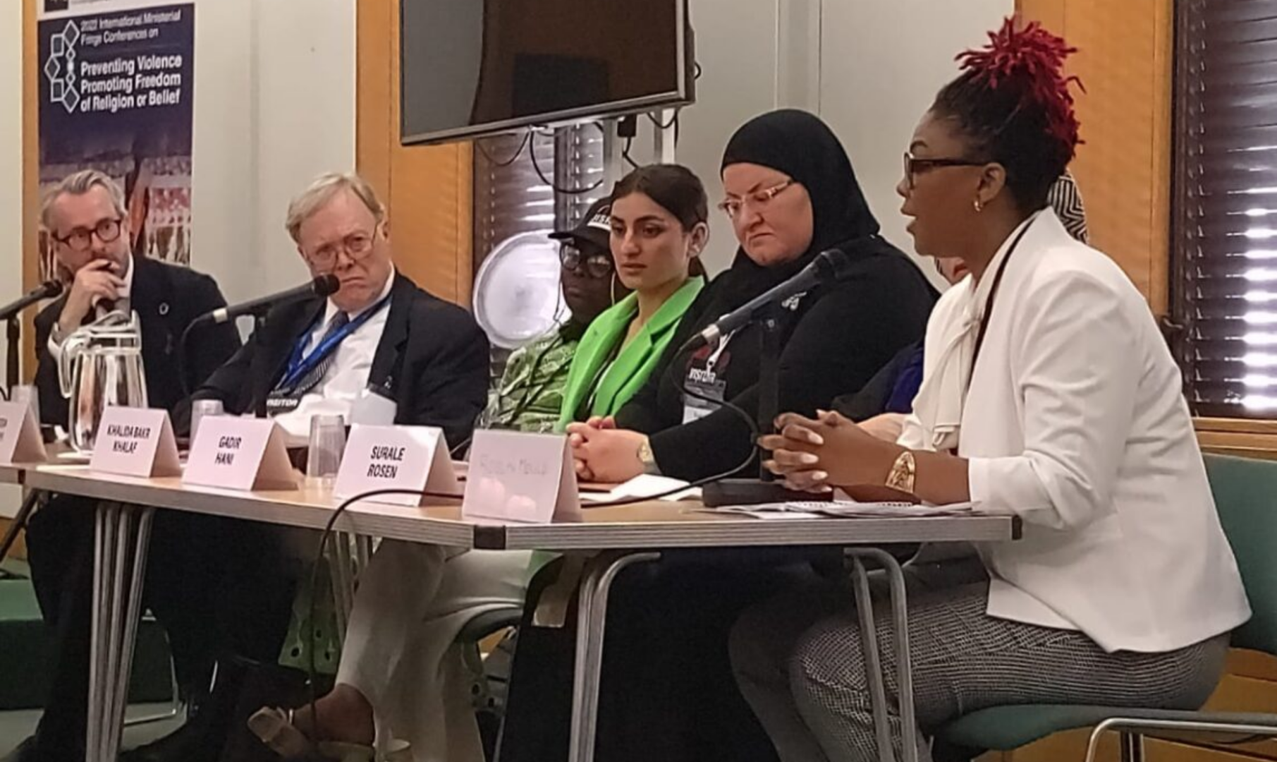 Rosyln speaking at a table with several speakers to her left, each with a name badge and microphone.